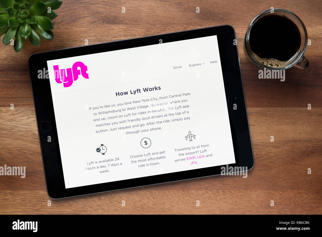 Il sito web di Lyft è visto su un tablet iPad, su di un tavolo di legno lungo con un caffè espresso e una pianta di casa (solo uso editoriale). Foto Stock