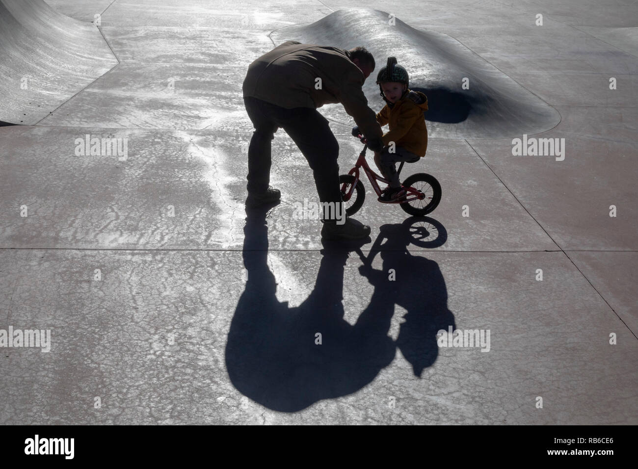 Denver, Colorado - Adam Hjermstad Suor aiuta il suo quattro-anno-vecchio figlio Adam Jr., a guidare il suo equilibrio bike in uno skatepark. Foto Stock