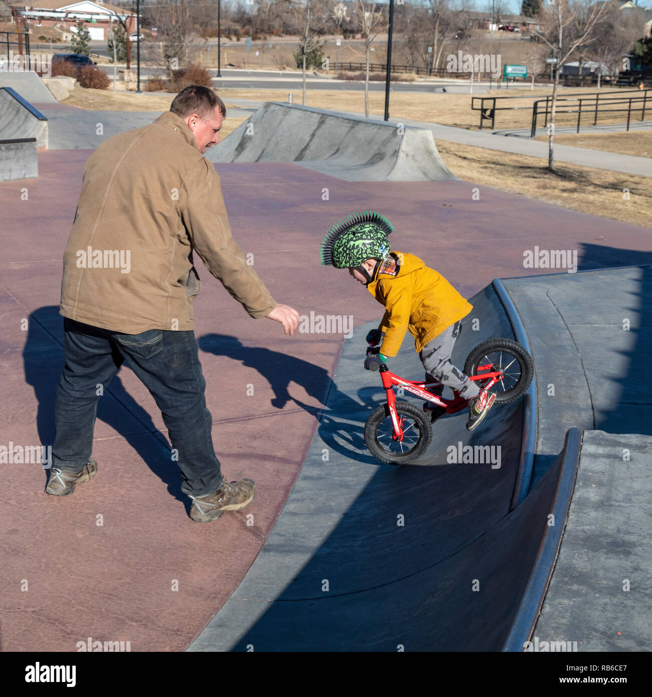 Denver, Colorado - Adam Hjermstad Suor aiuta il suo quattro-anno-vecchio figlio Adam Jr., a guidare il suo equilibrio bike in uno skatepark. Foto Stock