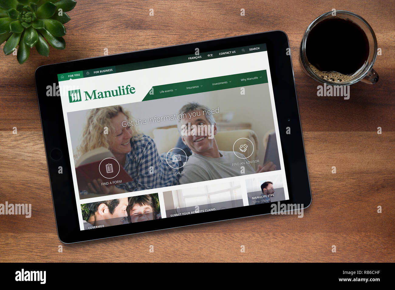Il sito web di Manulife è visto su un tablet iPad, su di un tavolo di legno lungo con un caffè espresso e una pianta di casa (solo uso editoriale). Foto Stock