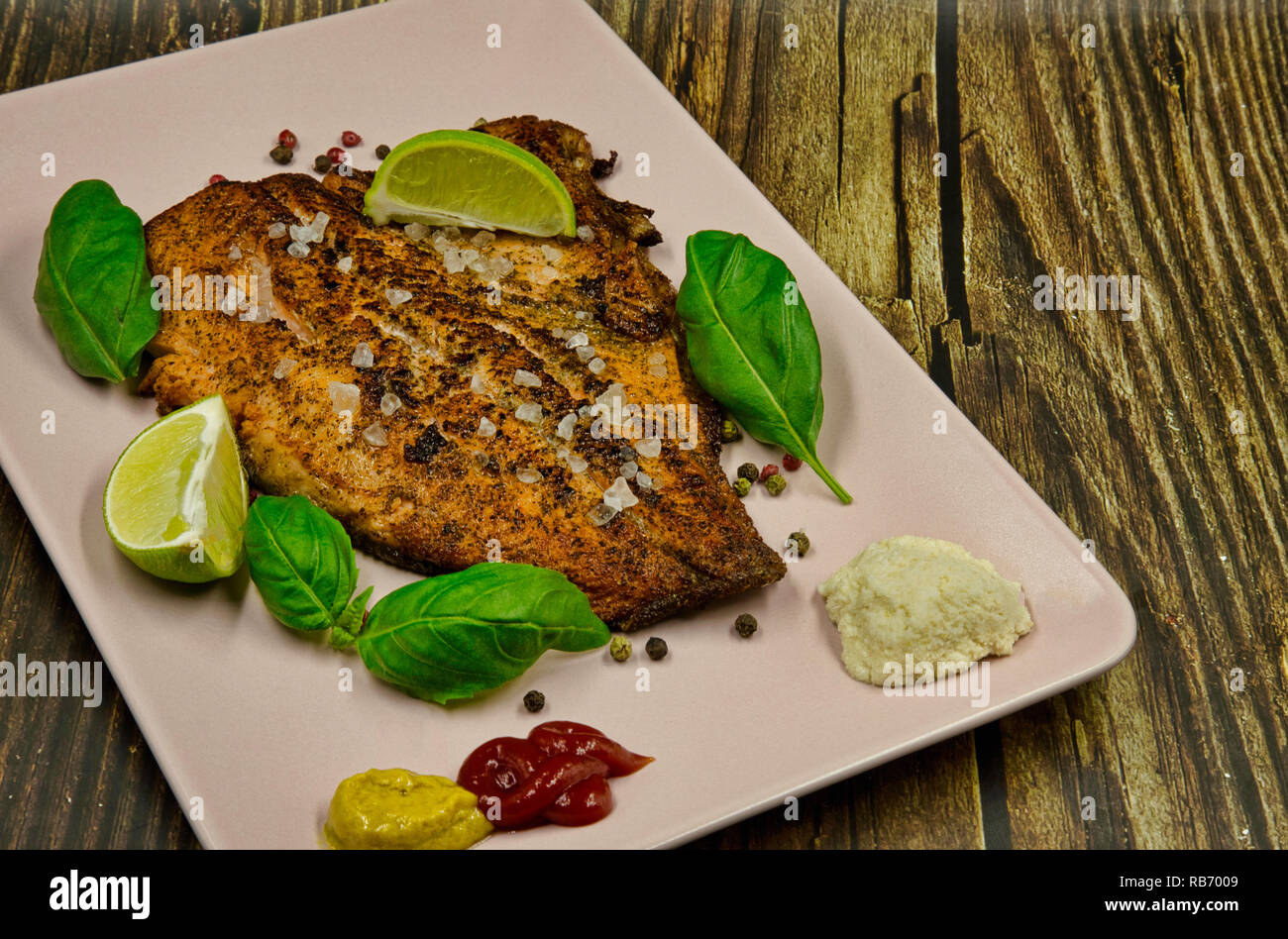 Fried rainbow-Bistecca al pepe con pepe, sale, senape e ketchup, guarnite con foglie di basilico e pezzi di calce, servita su un piatto di rosa. Appartamento , horizo Foto Stock