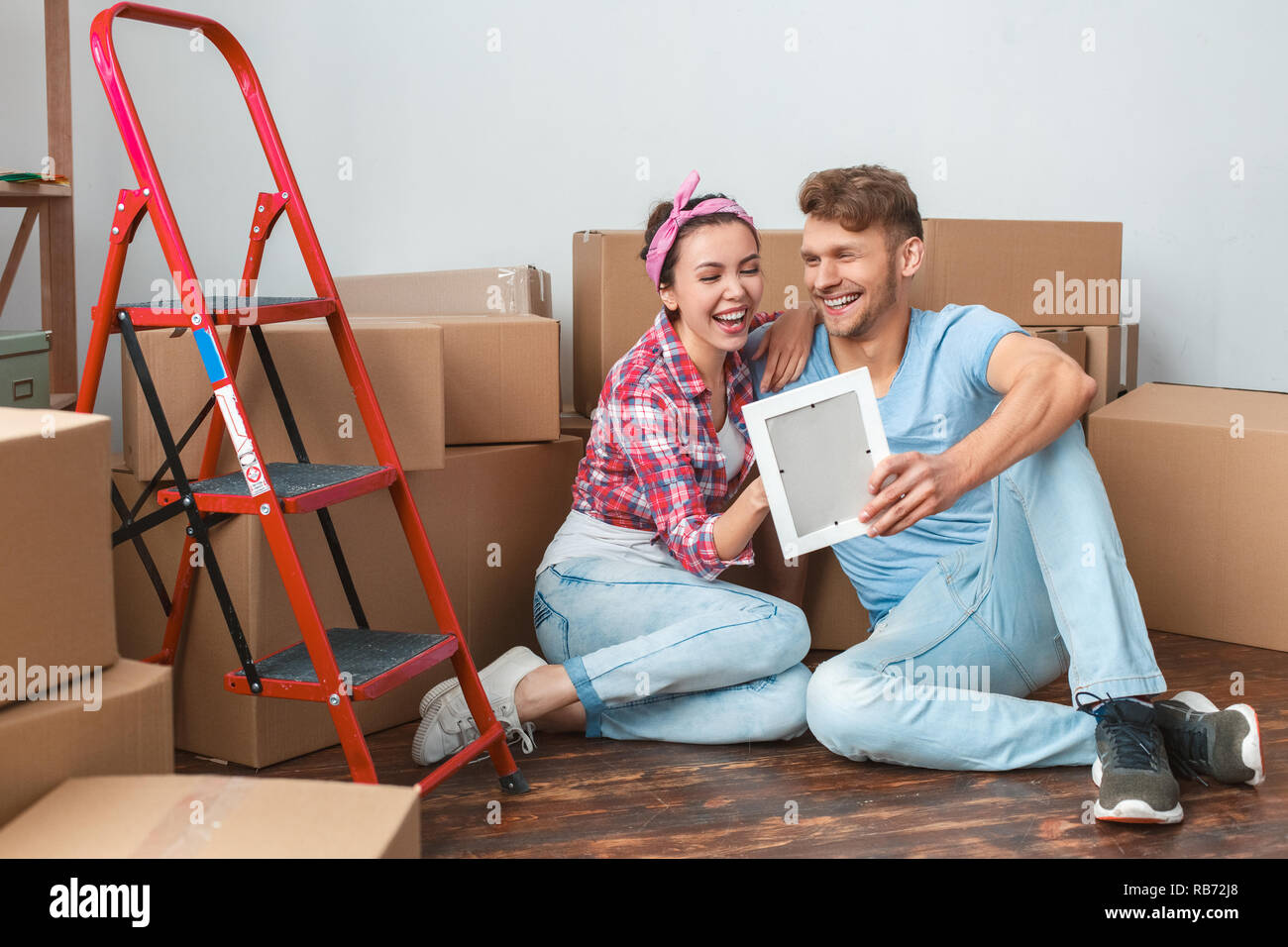Giovane marito e moglie di passare a nuovo luogo seduta sul pavimento abbracciava tenendo il photo frame ridendo allegro momento divertente Foto Stock
