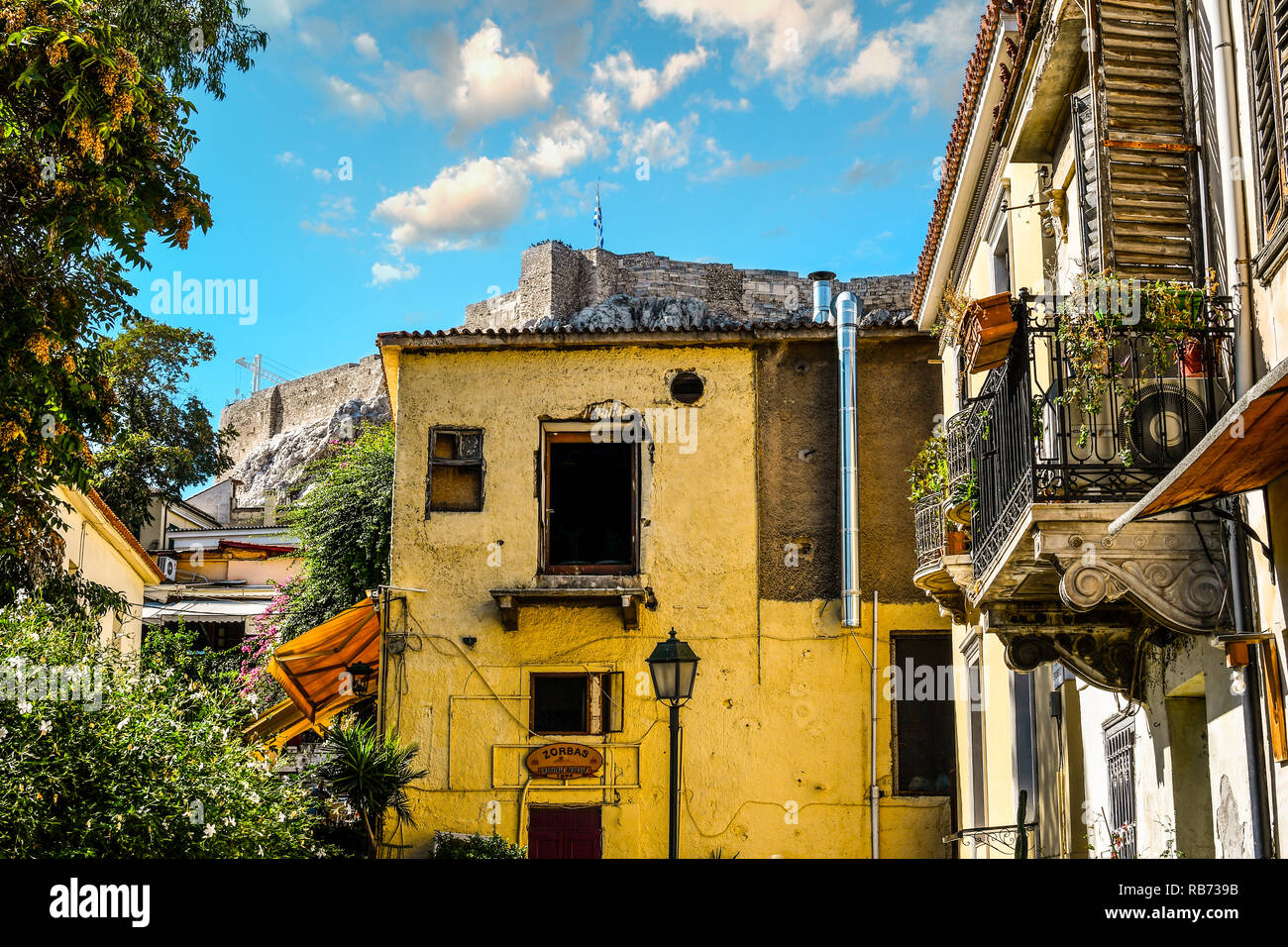 Rotto scavata windows in un vecchio edificio alla base del colle dell'acropoli come la bandiera greca vola sulla storica Acropoli di Atene in Grecia Foto Stock