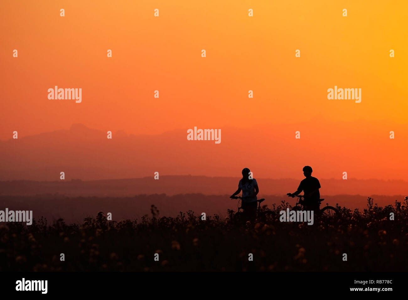 Donna e uomo fermano per ammirare la vista del tramonto mentre pedalano attraverso un parco urbano naturale sulla Nose Hill a Calgary, Canada Foto Stock