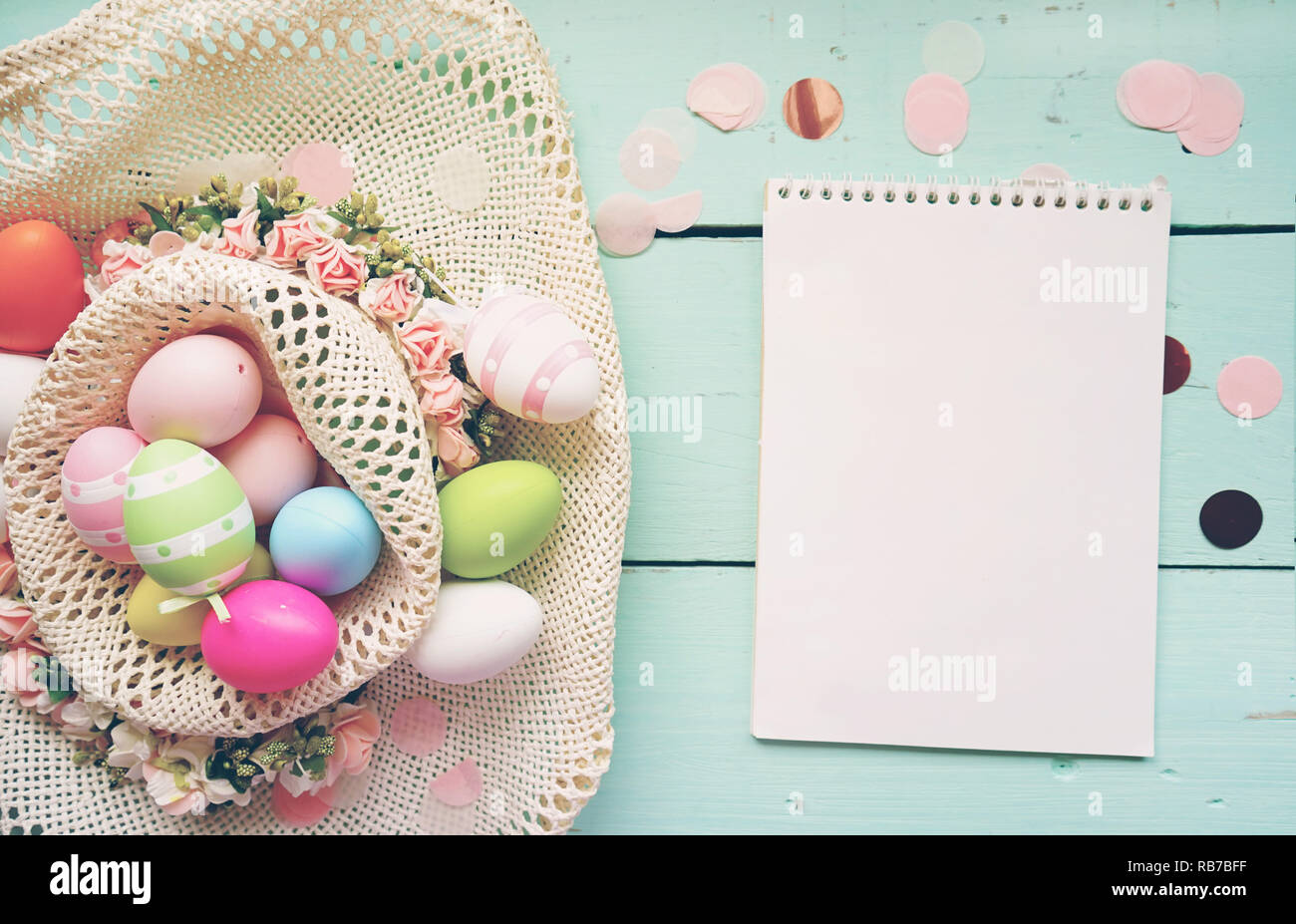 Un bello e colorato di close-up di piatto di uova di pasqua in semplici colori pastello e striato in un cestino con fiori da un notebook con uno spazio vuoto Foto Stock