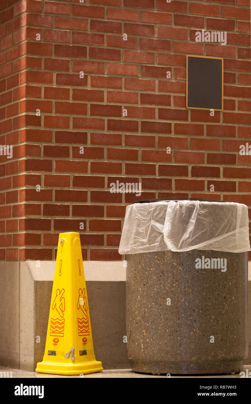 Contenitore di rifiuti e un pavimento bagnato contro il marcatore in rosso di un muro di mattoni Foto Stock