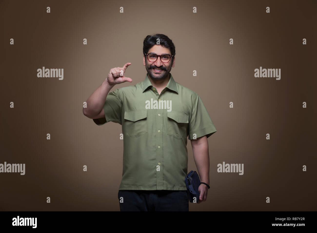 Uomo che indossa occhiali tenendo un piccolo sacchetto in una mano e mostra il gesto di contenimento di un prodotto con le dita. Foto Stock