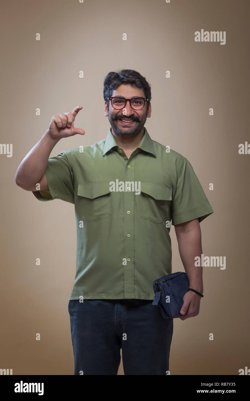 Uomo sorridente indossando occhiali tenendo un piccolo sacchetto in una mano e mostra il gesto di contenimento di un prodotto con le dita. Foto Stock
