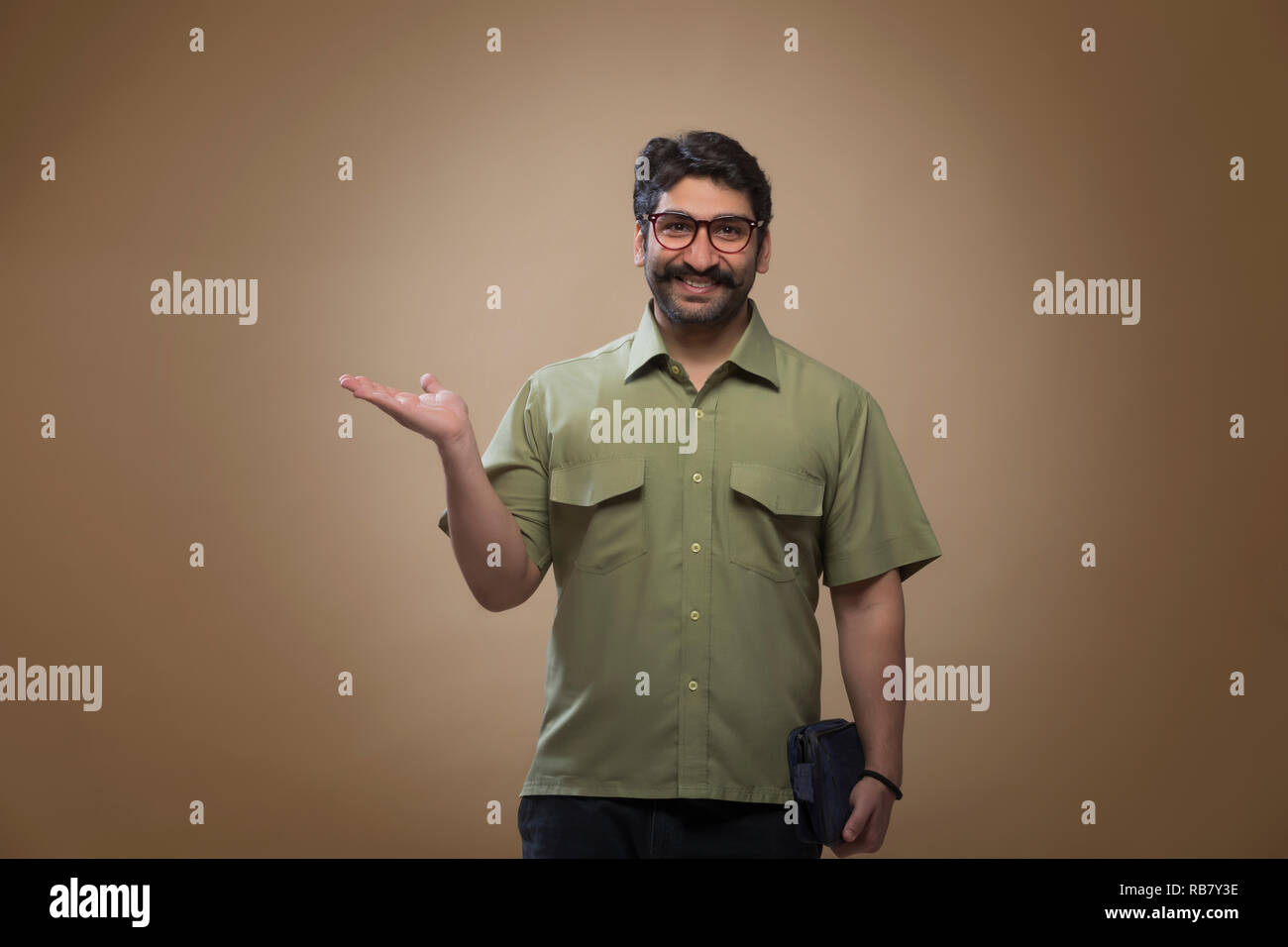 Uomo sorridente indossando occhiali tenendo un piccolo sacchetto in una mano e mostrando palm. Foto Stock