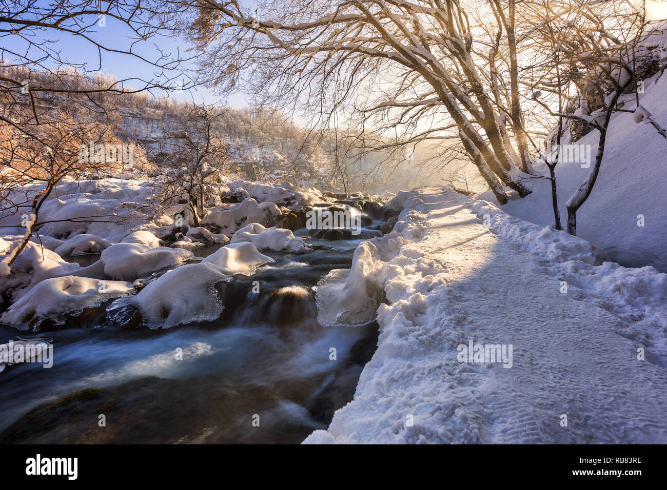 Percorso invernale coperto dalla neve e dal fiume che scorre attraverso il lago di Plitvice, Croazia Foto Stock