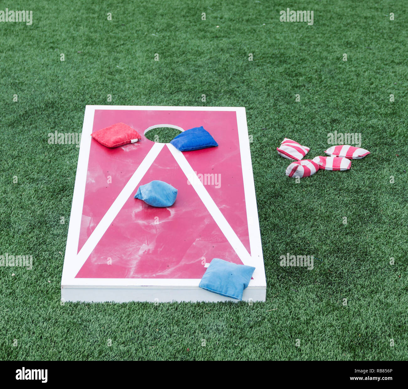 La riproduzione del popolare gioco foro di mais su un rosso e legno bianco con bordo blu e rosso striato sacchi di fagioli sul fondo erboso. Foto Stock