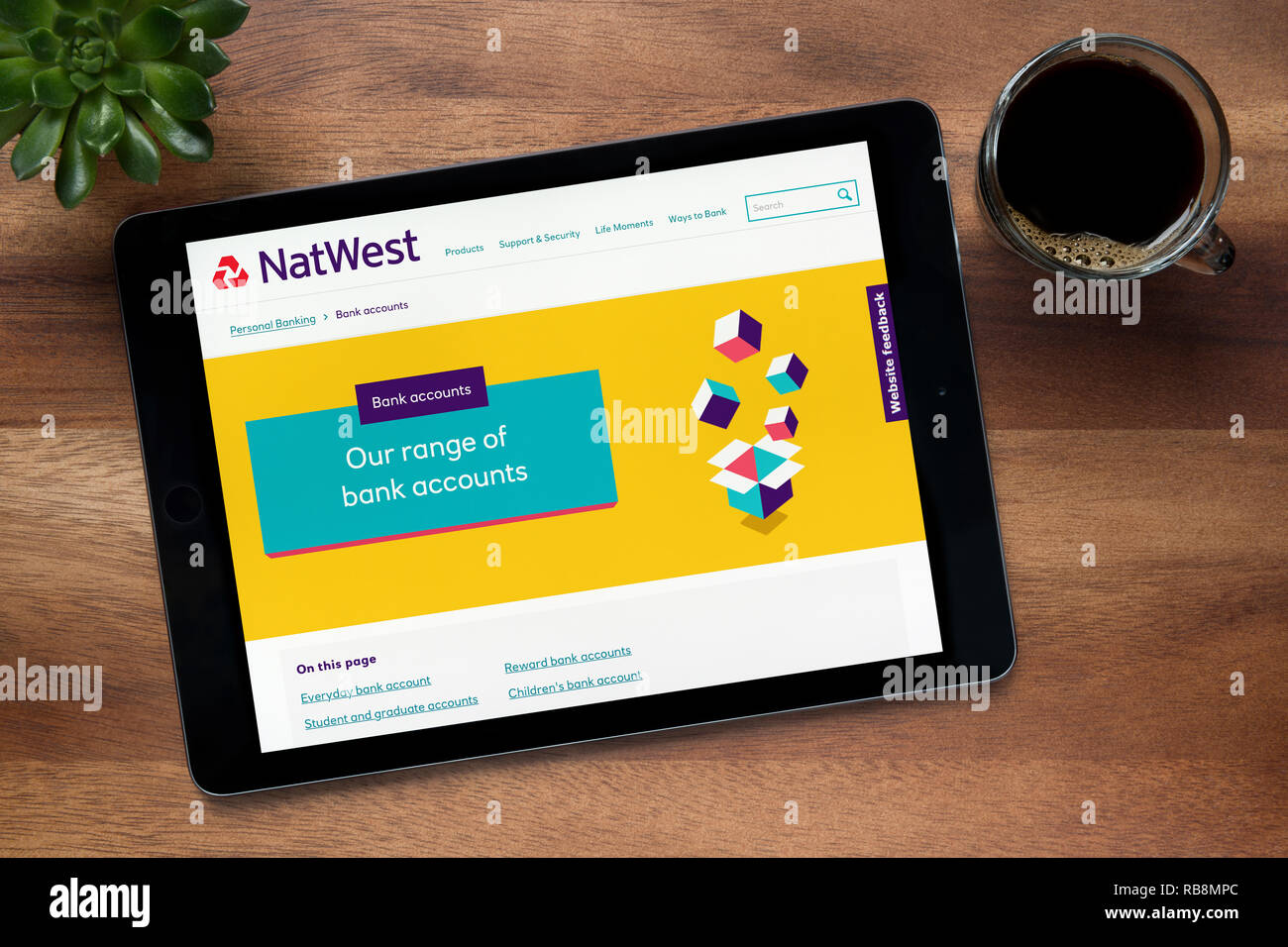 Il sito web di Natwest Bank è visto su un tablet iPad, su di un tavolo di legno lungo con un caffè espresso e una pianta di casa (solo uso editoriale). Foto Stock