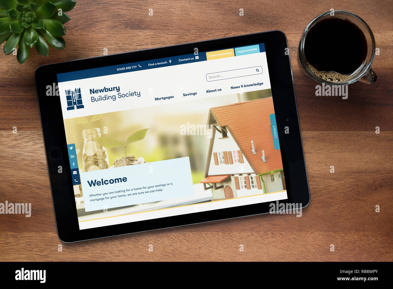 Il sito web di Newbury Building Society è visto su un tablet iPad, su di un tavolo di legno lungo con un caffè espresso e una pianta di casa (uso editoriale su Foto Stock