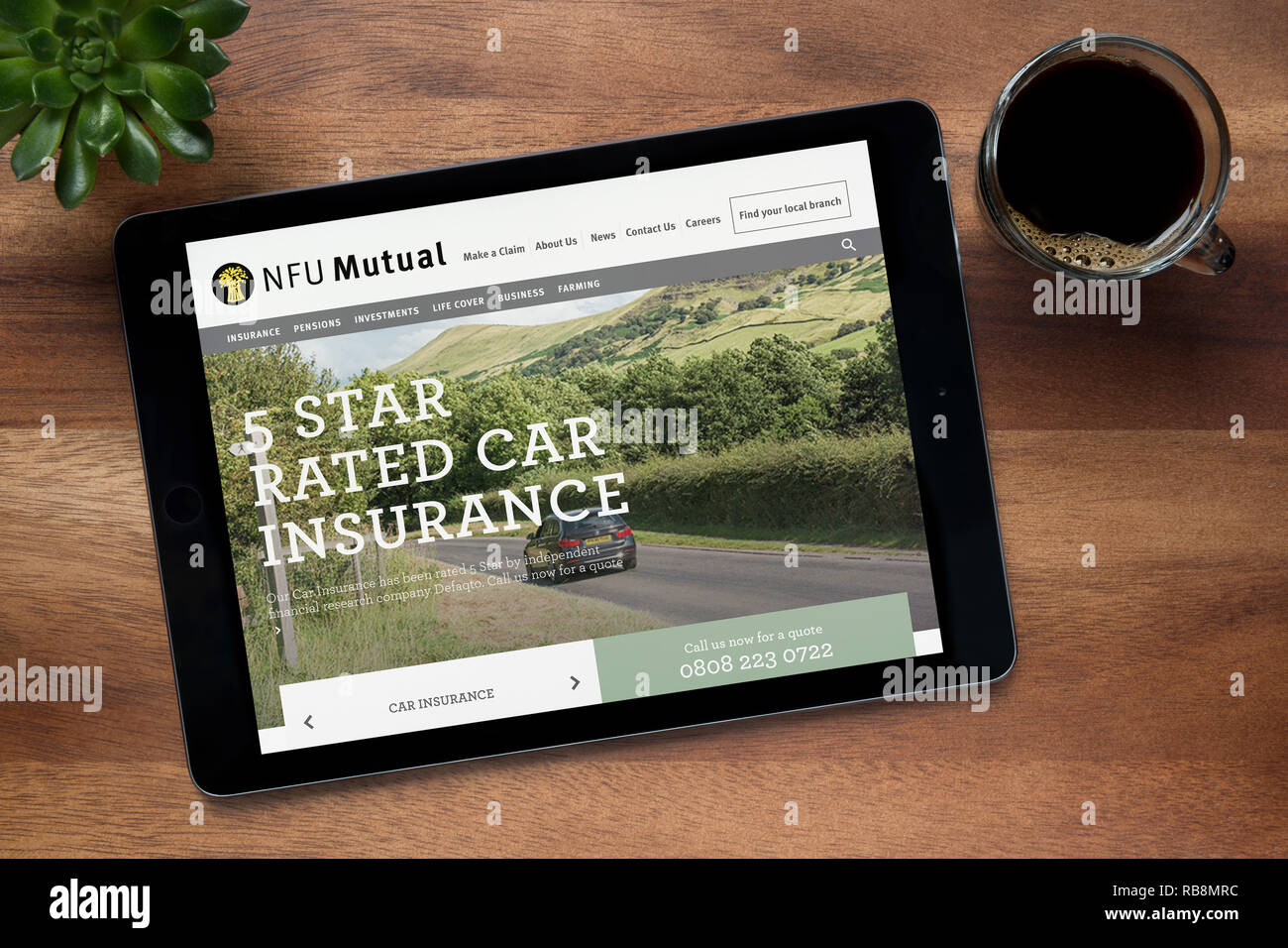 Il sito web della NFU mutuo è visto su un tablet iPad, su di un tavolo di legno lungo con un caffè espresso e una pianta di casa (solo uso editoriale). Foto Stock