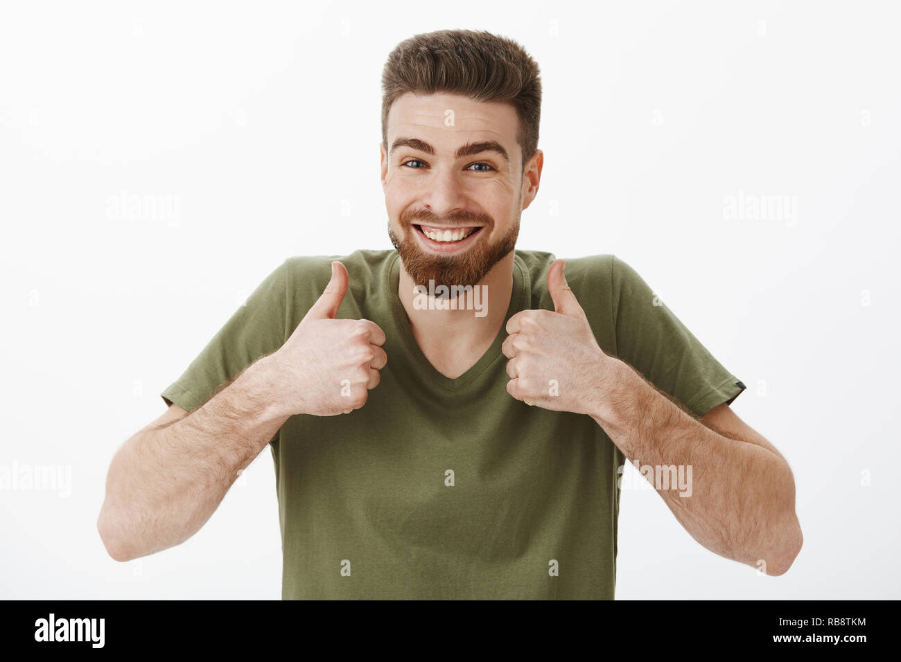 Al cento per cento sì. Ritratto di entusiasti felice upbeat attraente barbuto ragazzo caucasico in t-shirt alzando i pollici in su in approvazione e come gesto essendo allegro e solidale di accettare una buona idea Foto Stock