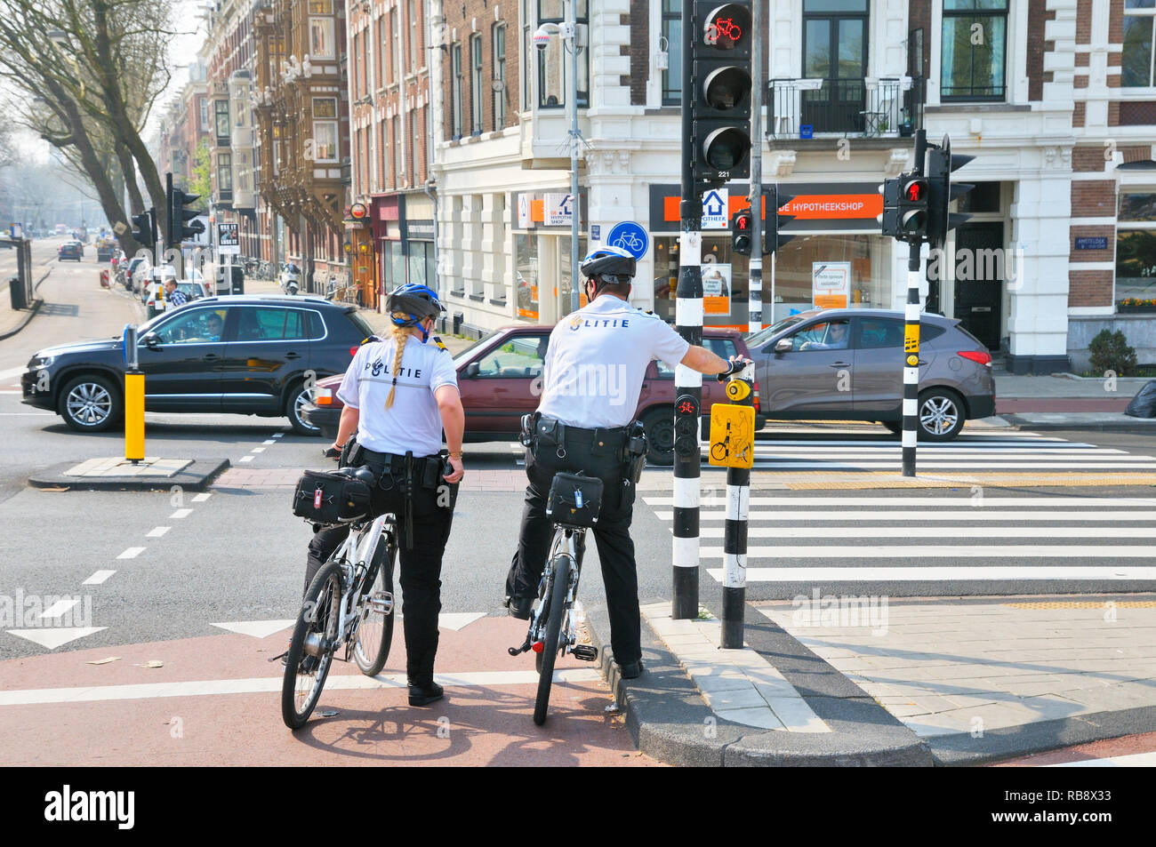 La polizia olandese ufficiali (politie) on bike patrol in attesa ad un semaforo, Amsterdam, Olanda Settentrionale, Paesi Bassi Foto Stock