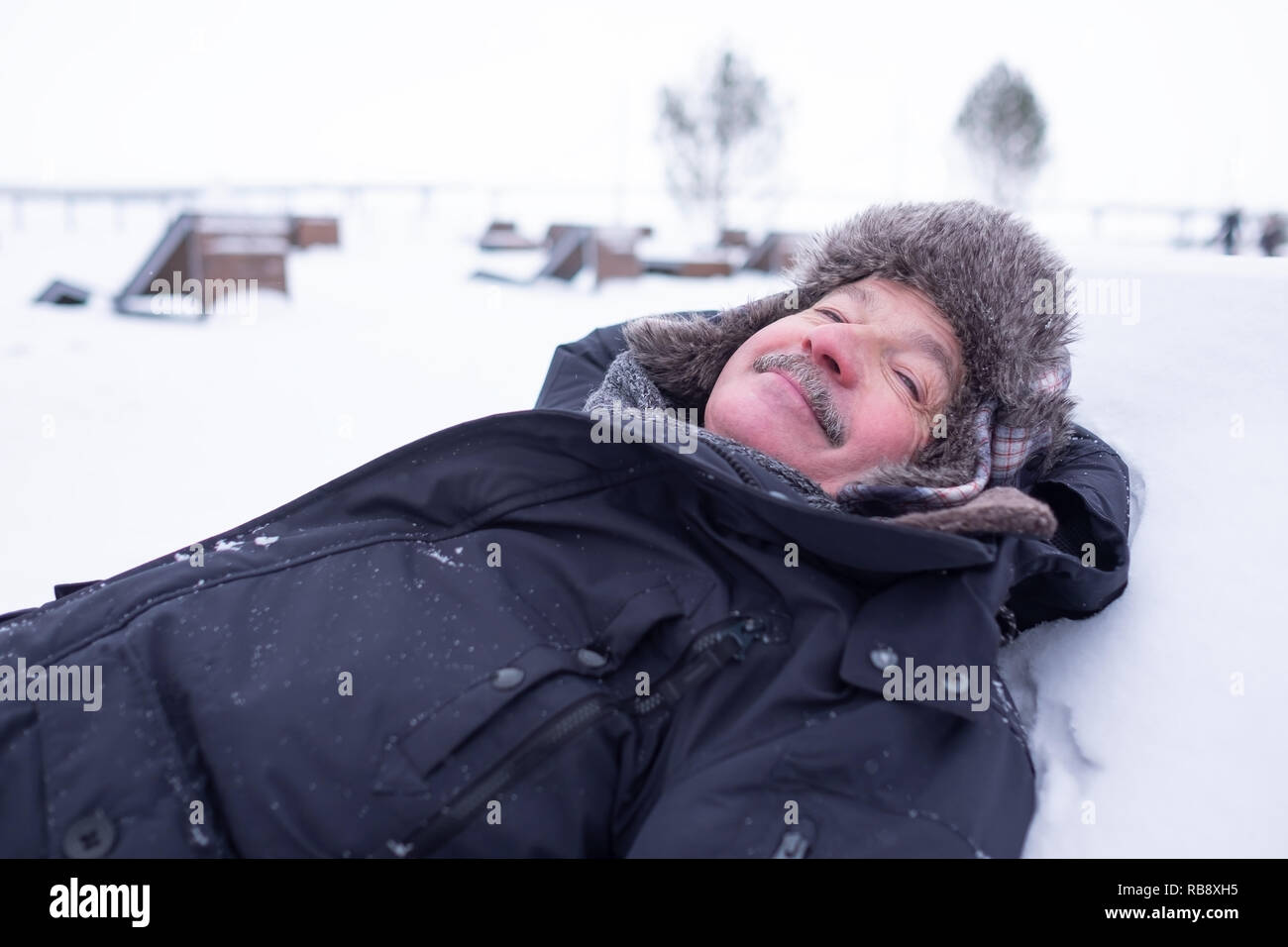 Senior uomo bello in vestiti caldi e hat giacente sulla neve di sognare e divertirsi Foto Stock