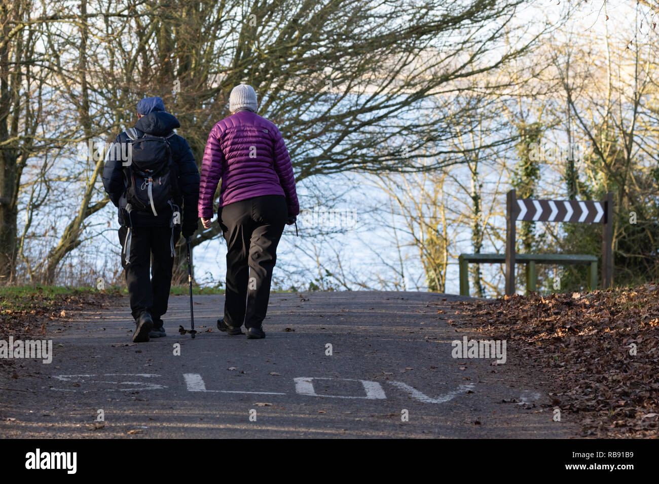 Draycote, Warwickshire / UK - Gennaio 2019: un uomo e una donna, le spalle alla telecamera a piedi lungo una strada su cui la parola 'Slow' è dipinta. Foto Stock