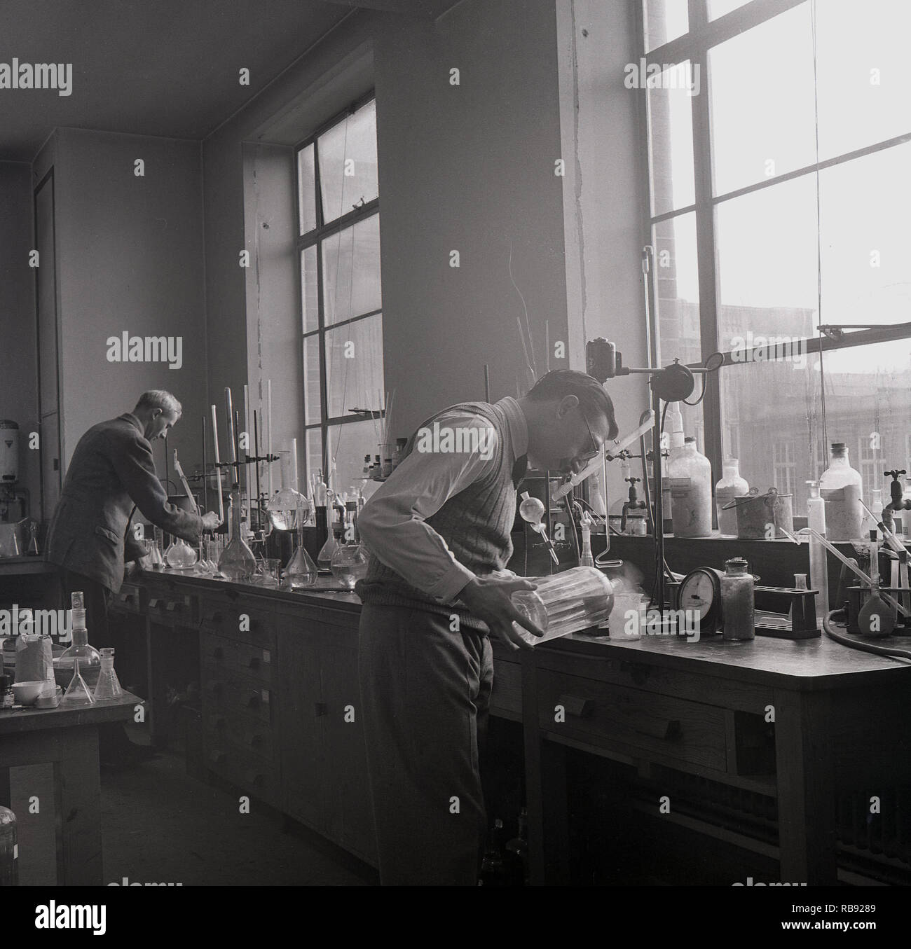 Degli anni Cinquanta, storico, due maschio gli scienziati che lavorano con prodotti chimici in corrispondenza di un banco in un laboratorio di chimica dell'Università di Oxford, Inghilterra, Regno Unito. Foto Stock