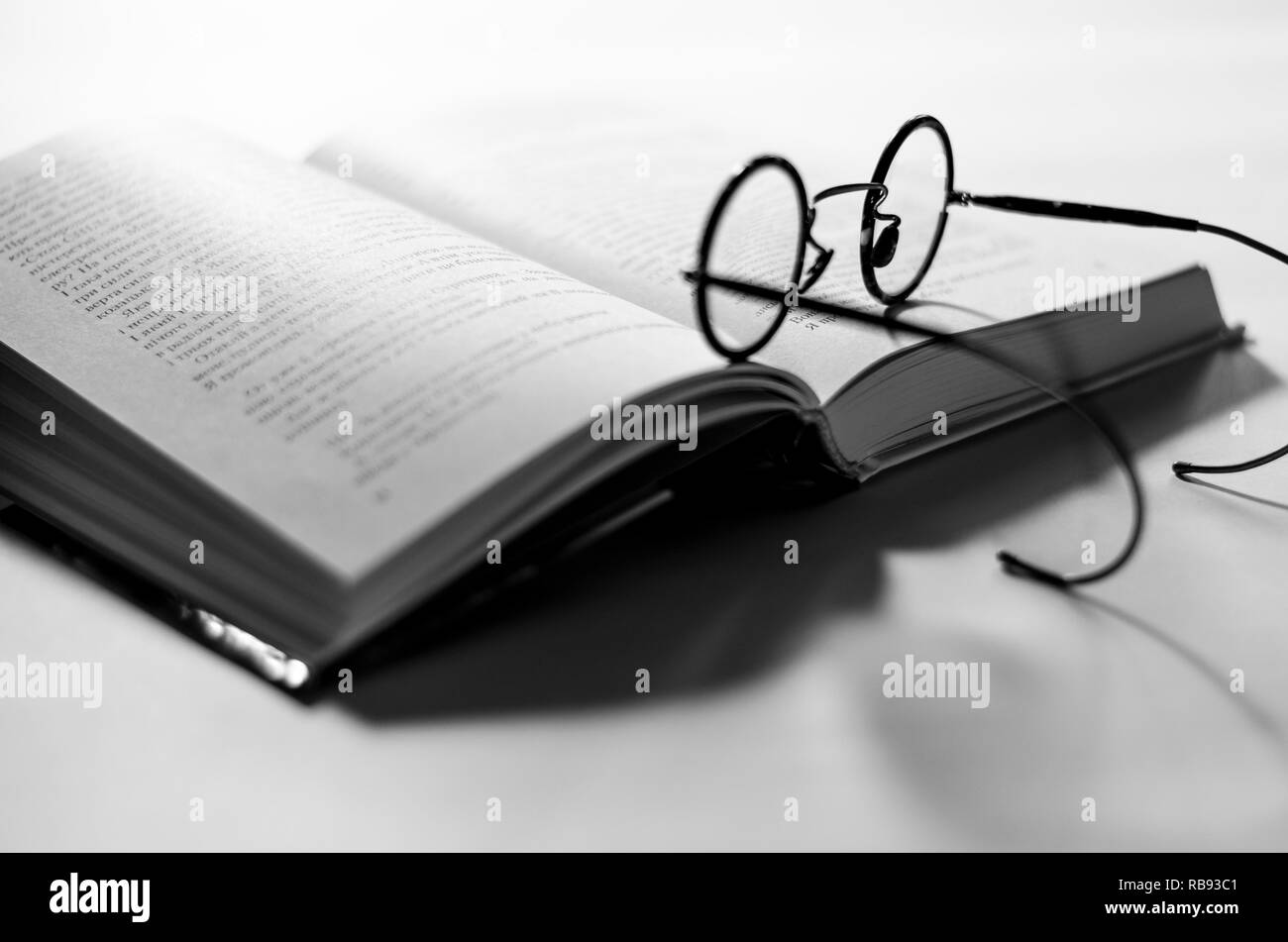 Nero tondo i vecchi occhiali giaceva su un aperto il libro bianco si trova su sfondo bianco Foto Stock