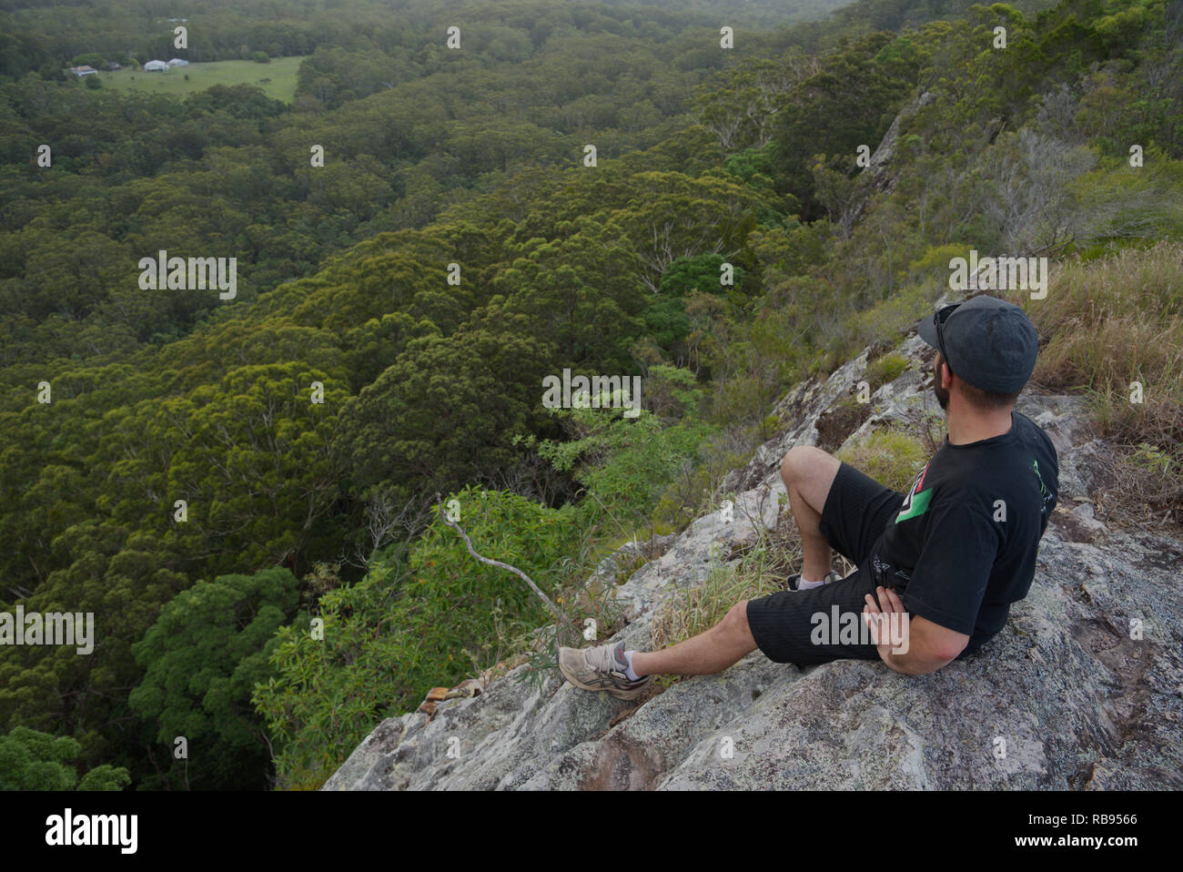 Uomo seduto sul bordo di una scogliera sulla parte superiore di una foresta Foto Stock