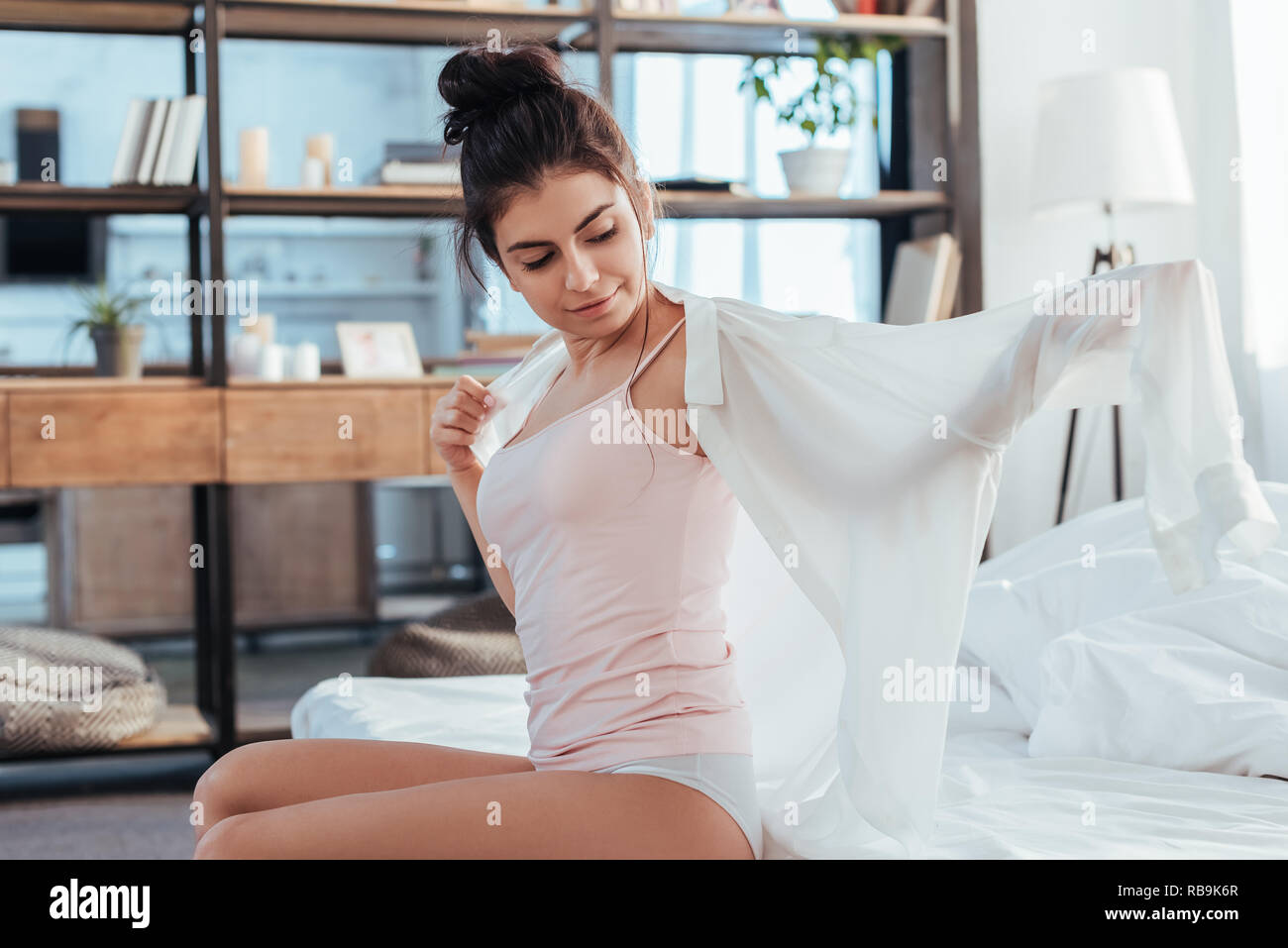 Felice giovane donna mettendo su una camicia bianca durante la mattina tempo a casa Foto Stock