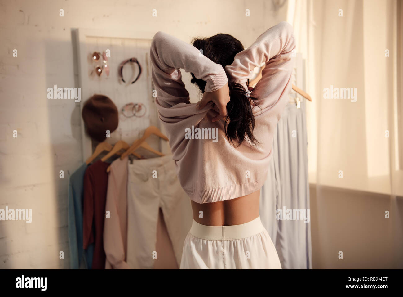 Vista posteriore della giovane donna mettendo su eleganti maglione a casa Foto Stock