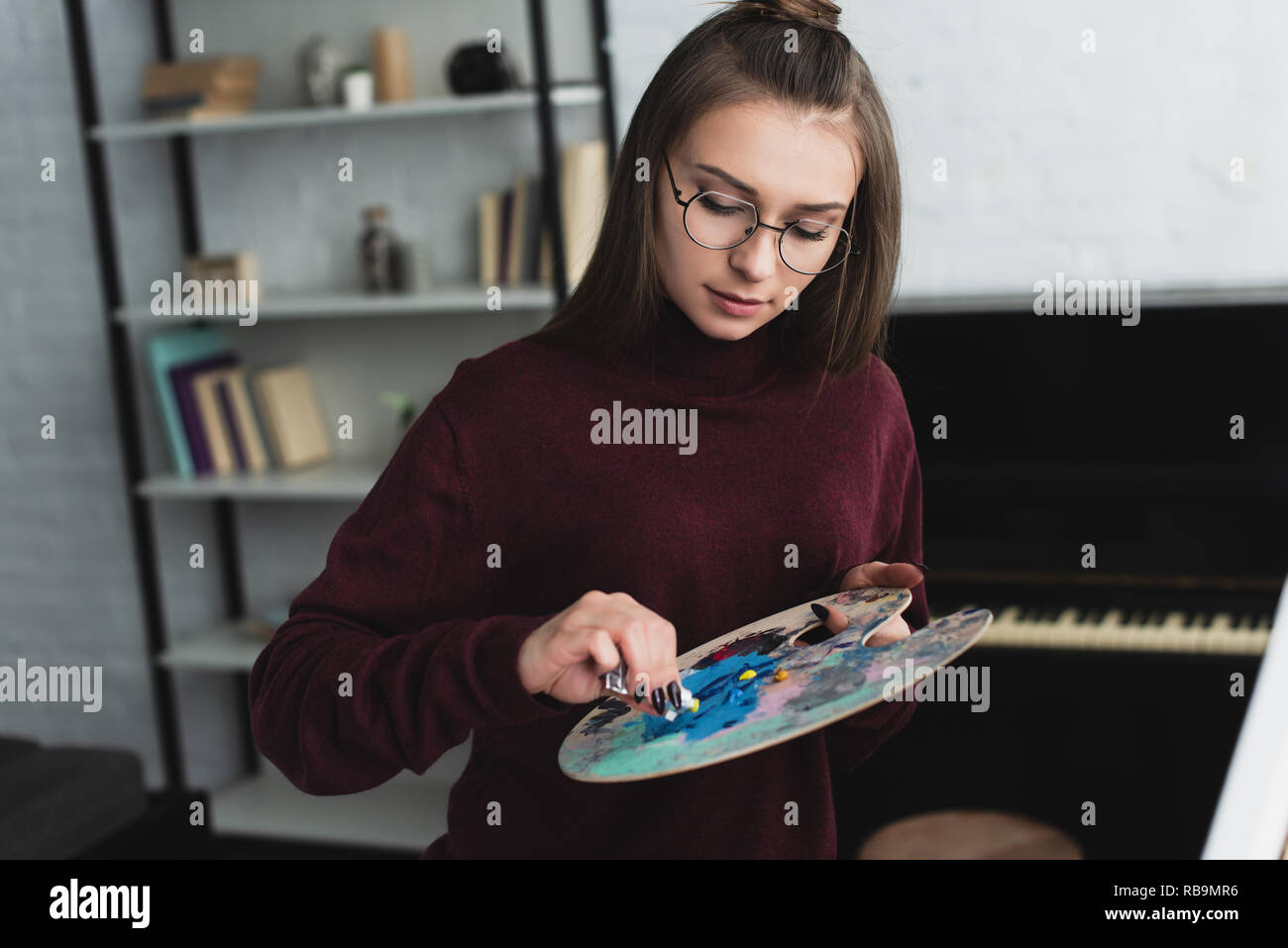 Ragazza in Borgogna maglione con palette seduto e pittura a casa Foto Stock