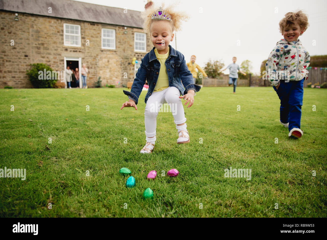 I bambini che eseguono come la ricerca con entusiasmo per le uova di Pasqua di cioccolata. Foto Stock