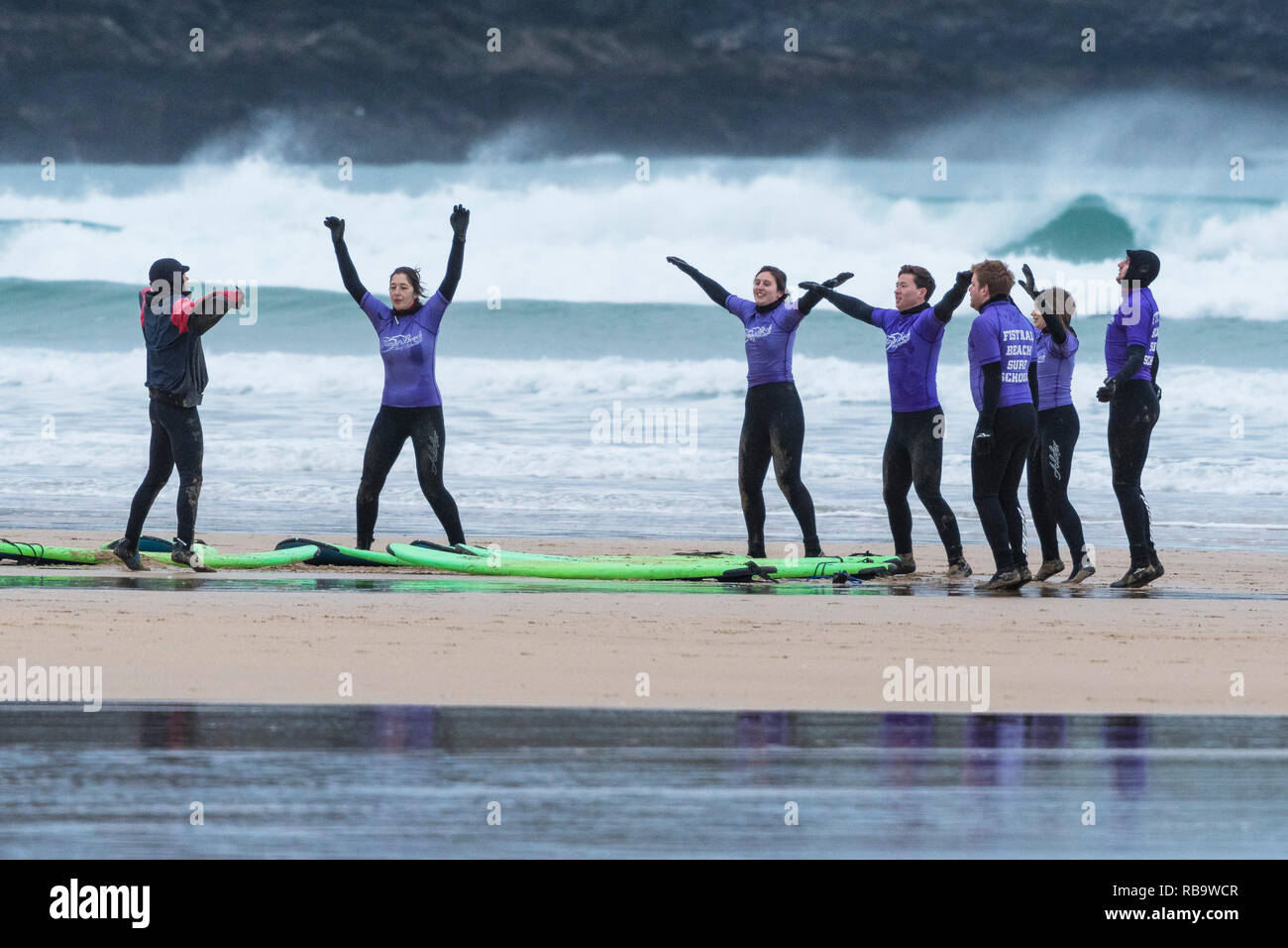 I surfisti principianti in fase di riscaldamento con il loro istruttore all'inizio di una lezione di surf a Fistral Beach in Newquay Cornwall. Foto Stock