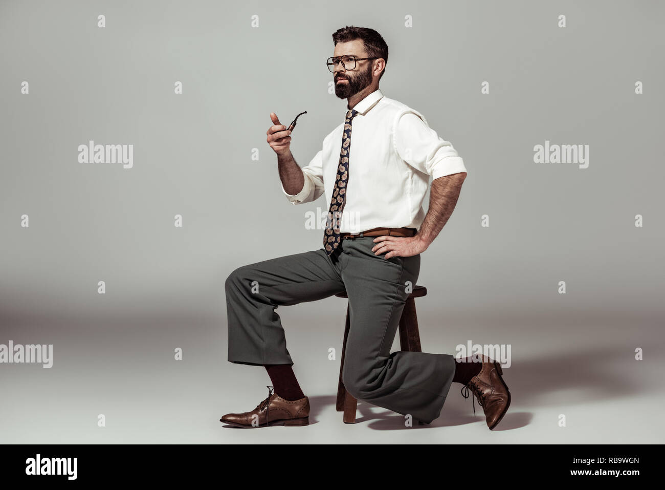 Bel uomo barbuto in bicchieri seduti su una sedia e tubo di contenimento Foto Stock