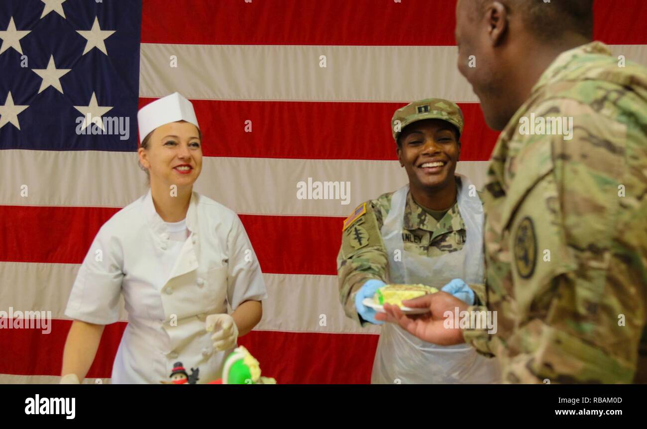 Esercito degli Stati Uniti Capt. Rayvon Stanley, con gli Stati Uniti Army Medical attività di reparto la Baviera, serve la torta di soldati durante la cena di Natale a Mihail Kogălniceanu, Romania, 25 dicembre, 2018. Stati Uniti I soldati dell esercito celebrare le vacanze e costruire relazioni durature con i loro alleati e partner della NATO a sostegno dell'operazione Atlantic risolvere. Foto Stock