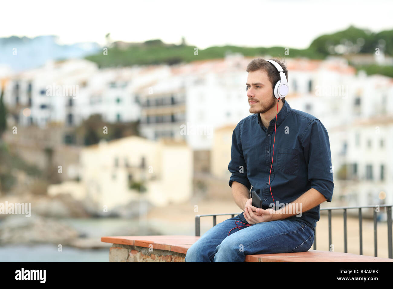 Grave uomo ascoltare musica dal telefono intelligente sititng su una battuta in vacanza Foto Stock