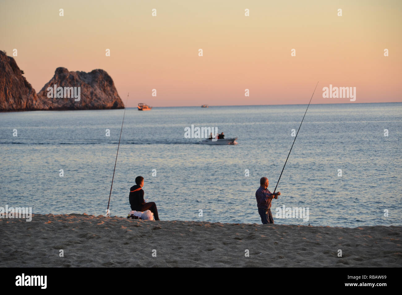 Alanya, Turchia, 29 ottobre 2018: I pescatori pescano lungo la spiaggia di Cleopatra durante un tramonto dorato, con il cielo bagnato dalle calde sfumature serali. Foto Stock