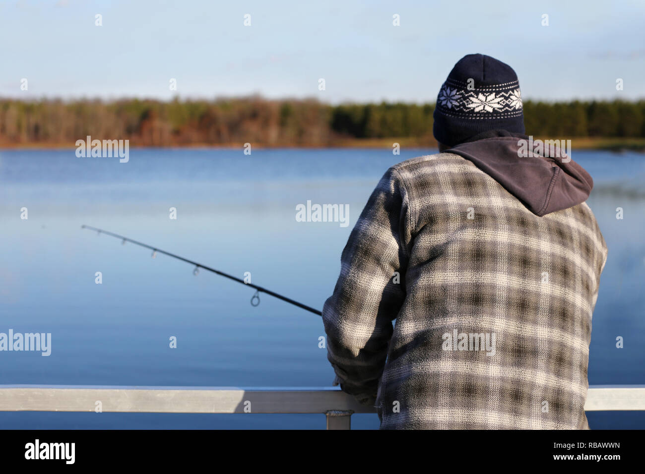 Un uomo è preinstallato in vestiti caldi mentre la pesca al largo una dock su un piccolo lago artificiale nel midwestern Stati Uniti in una fredda giornata. Foto Stock