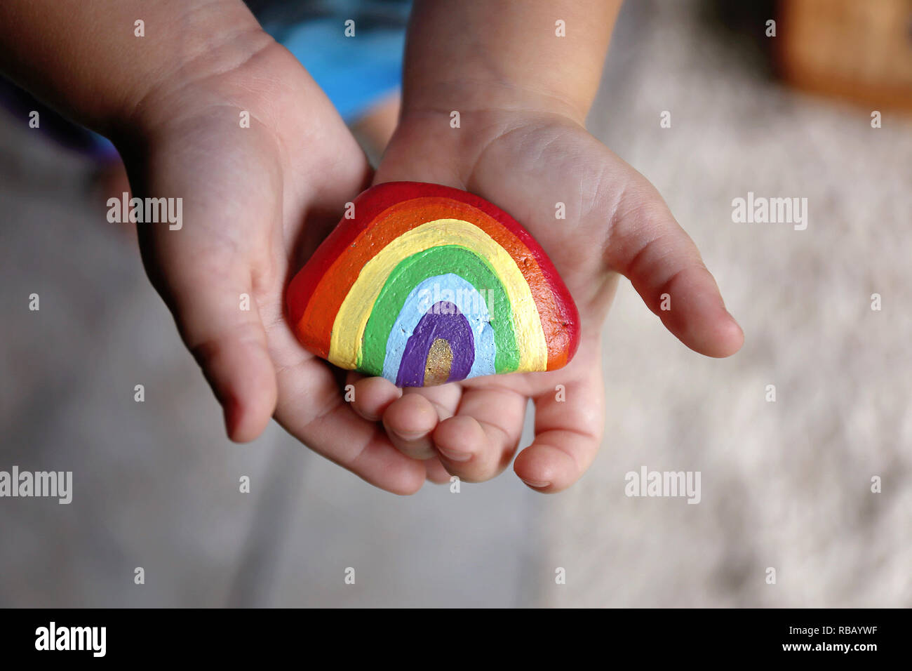 Le mani di un giovane bambino bambino sono dolcemente tenendo un acrilico verniciato rainbow rock. Foto Stock