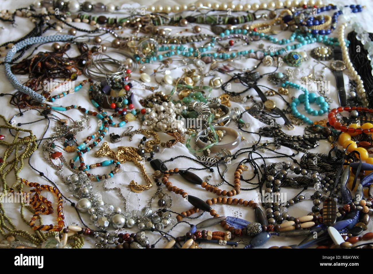 Gioielli. Una collezione di gioielli steso su un letto con un foglio bianco. Jewells. Gli oggetti di valore. Beni personali. Valore sentimentale. Pietre. Perle. Perline. Collane. Braccialetti. Un orologio da polso. Multi colorata. Assortimento. Foto Stock