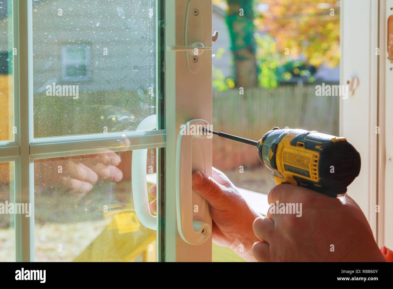 Installare la maniglia della porta con una serratura, falegname serrare la vite utilizzando un trapano elettrico cacciavite, close-up. Foto Stock