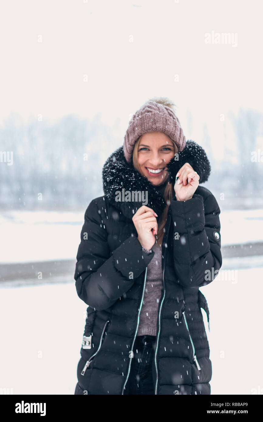 Donna sorridente in tempo freddo mentre la caduta della neve. Foto Stock