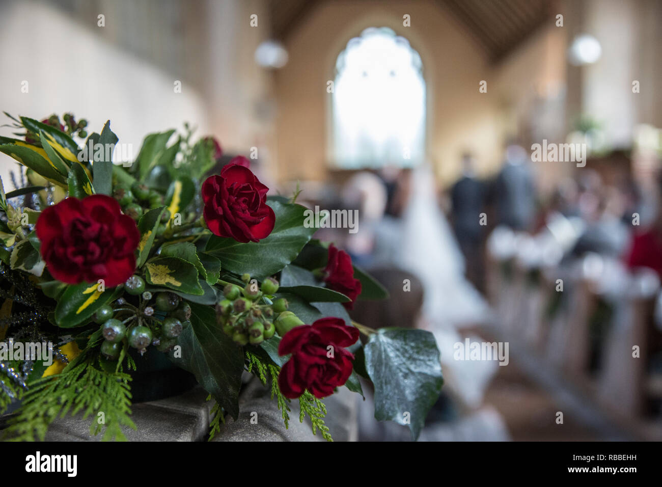 Garofani rossi in bouquet in chiesa un giorno di nozze con la sposa e lo sposo in soft focus in background sul loro giorno di nozze Foto Stock