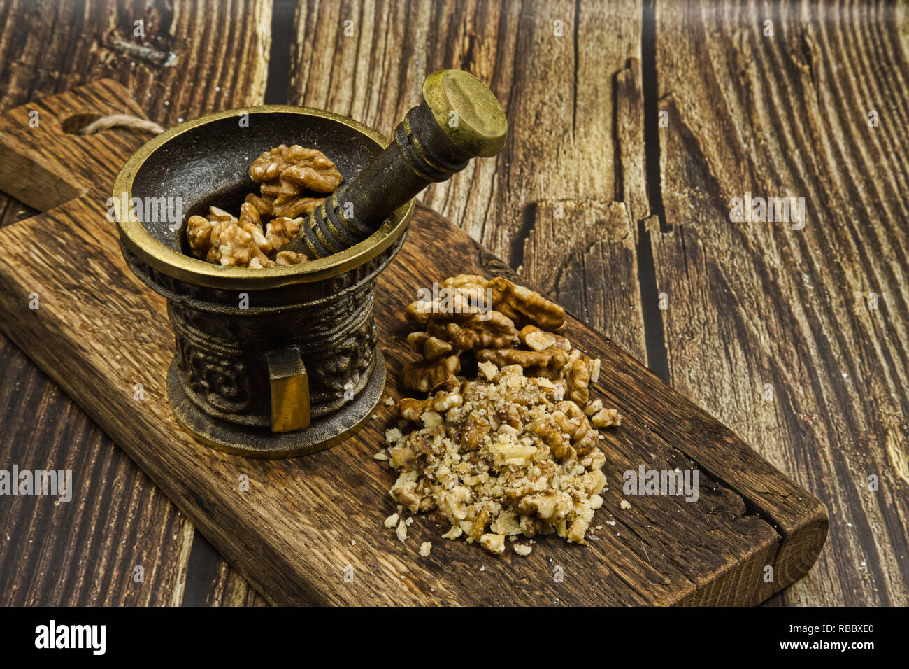 Vecchio mortaio con pestello e noci intere e grattugiato sulla vecchia sfondo in legno in stile vintage.Close, vista orizzontale. Foto Stock