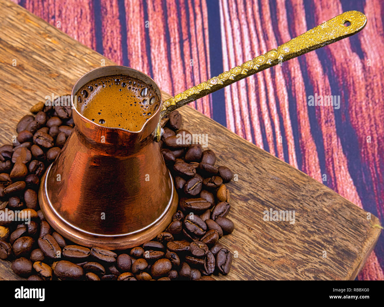 Forte colore nero caffè servito in un vecchio rame crogiolo su una vecchia tavola di legno, i chicchi di caffè intorno a. Chiudere, orizzontale piana, vista in pianta da sopra Foto Stock