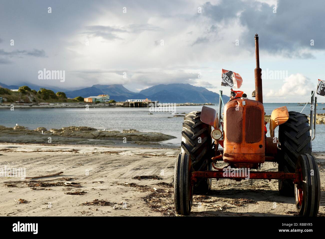 Un vecchio trattore vintage siede su un trova sabbia spiaggia vicino a Baia Mare. Montagne sullo sfondo e la raccolta di nuvole con un impianto di pesca. Foto Stock