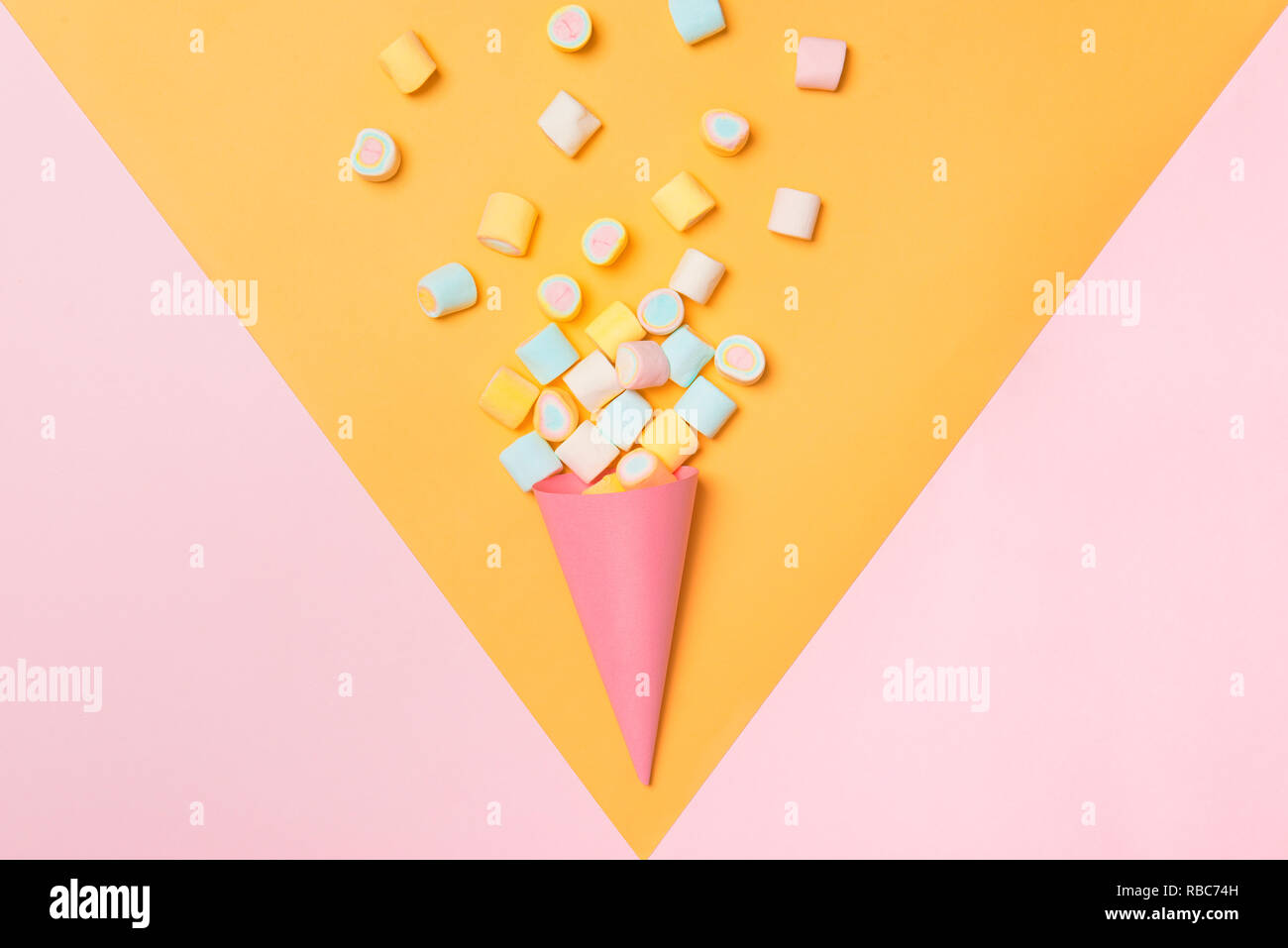 Marshmallow candy colorato assortimento in un cono gelato in rosa e sfondo giallo visto dal di sopra. Caramelle gommose variazione. Vista superiore Foto Stock