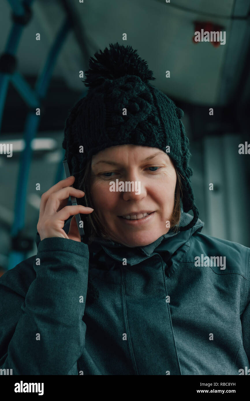 Bella donna adulta parlando al telefono cellulare in bus pubblico in inverno freddo pomeriggio Foto Stock