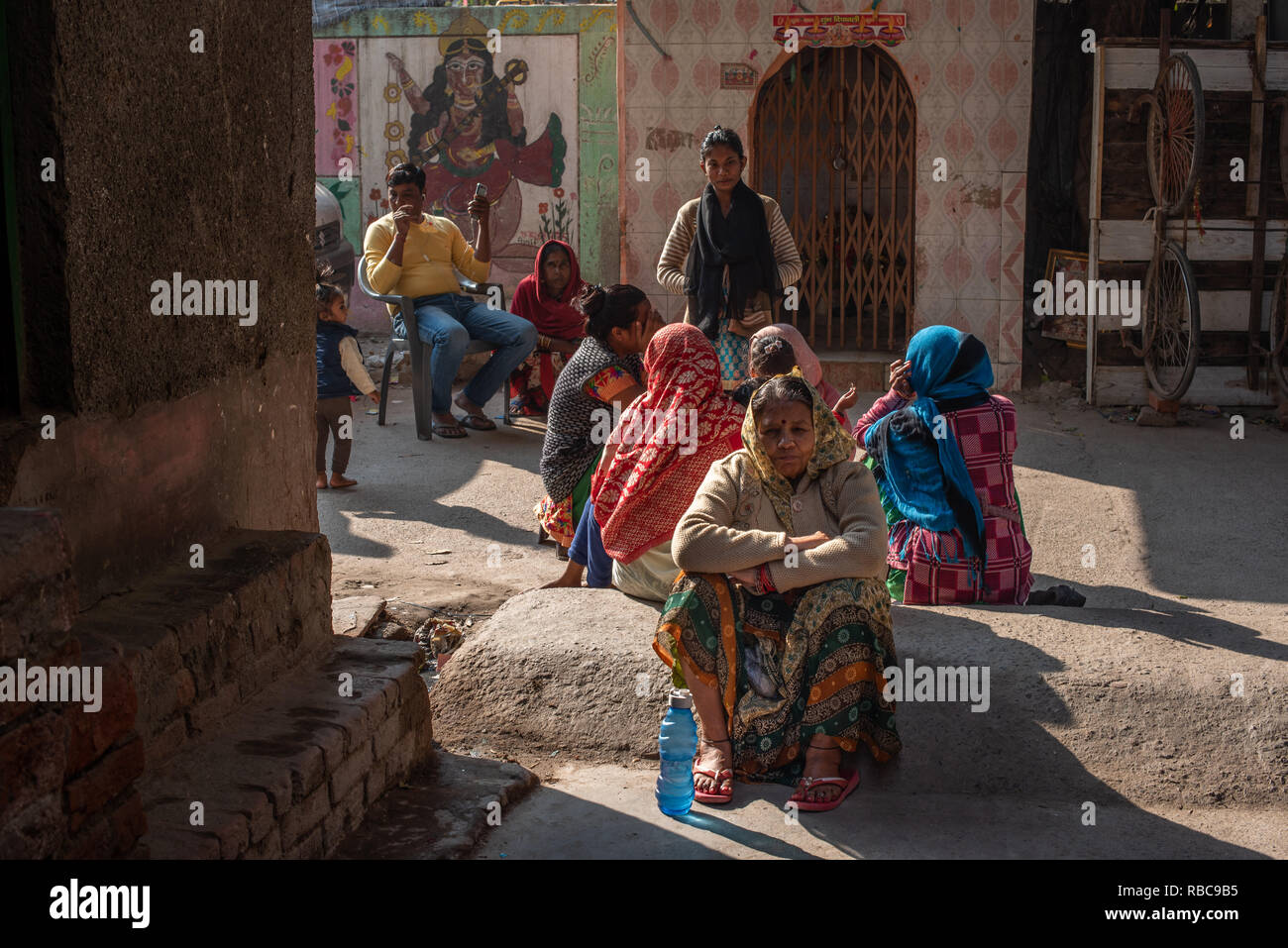 La vita sulle strade su un wintery pomeriggio soleggiato nella colonia di JJ Madanpur Khadar, Nuova Delhi - gruppo di donne insieme seduto davanti a un tempio. Foto Stock