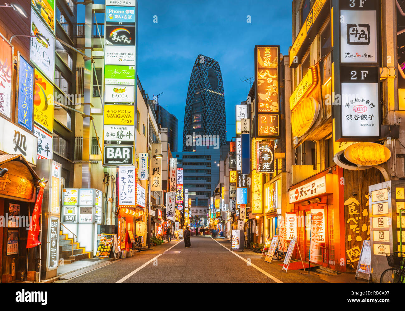 Shinjuku, Tokyo, regione di Kanto, Giappone. Illuminati segni al neon al crepuscolo e Cocoon Tower in background. Foto Stock