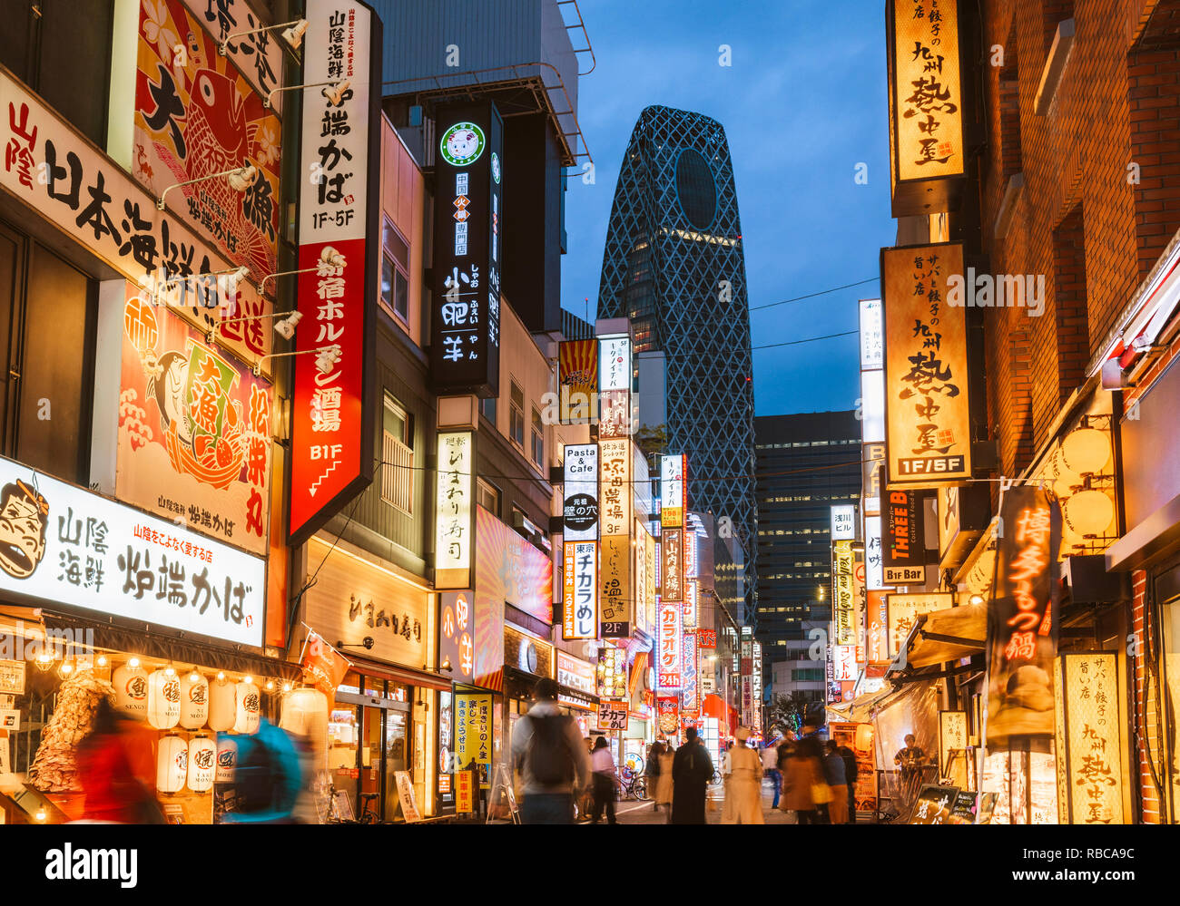 Shinjuku, Tokyo, regione di Kanto, Giappone. Illuminati segni al neon al crepuscolo e Cocoon Tower in background. Foto Stock