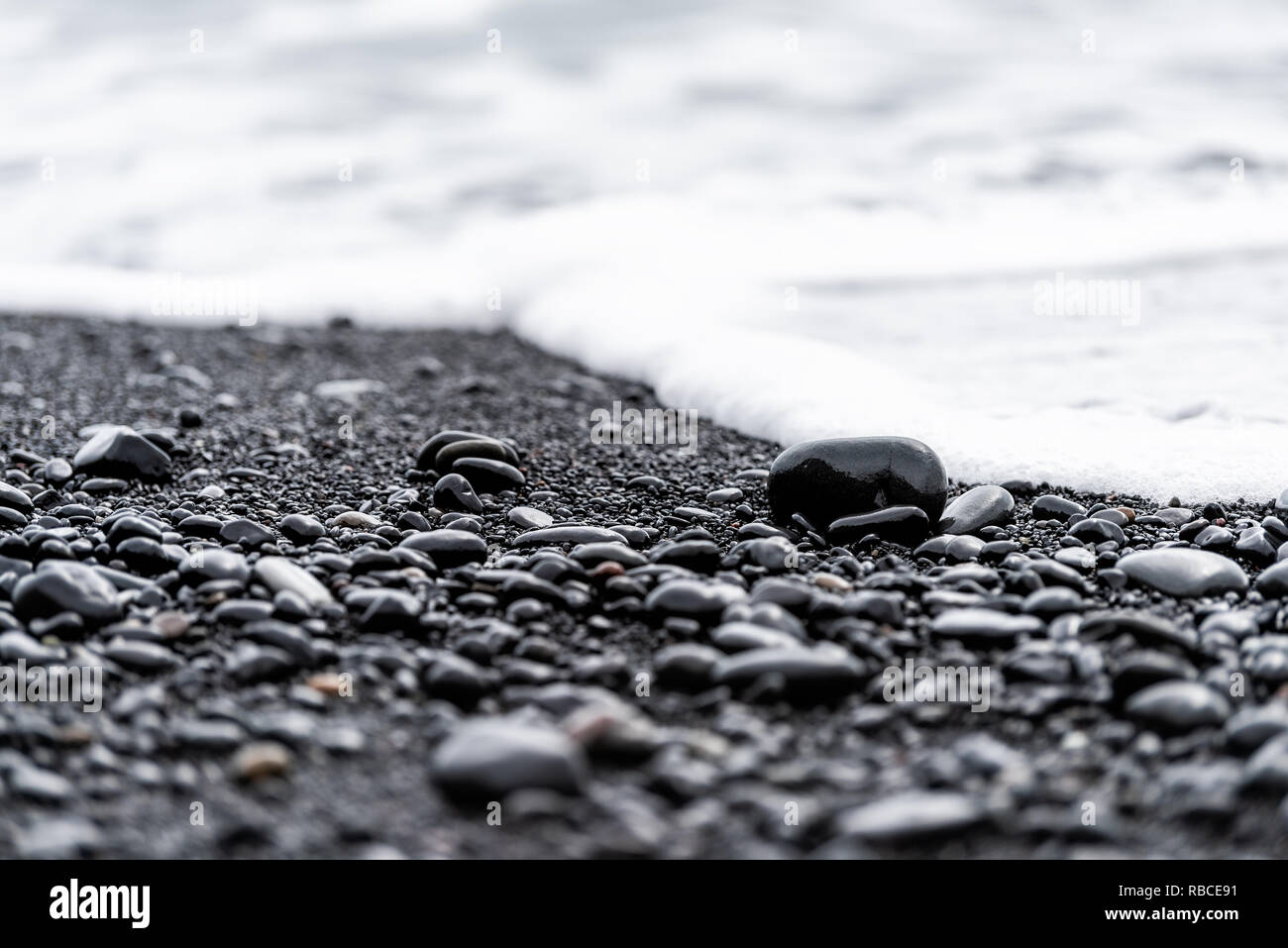 Primo piano della grande nero pietre vulcaniche o granelli di sabbia sulla spiaggia di Reynisfjara, Islanda con acqua onde che si infrangono sulla riva a lucido rocce umide Foto Stock