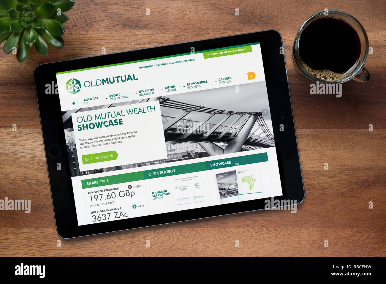 Il sito web di Old Mutual è visto su un tablet iPad, su di un tavolo di legno lungo con un caffè espresso e una pianta di casa (solo uso editoriale). Foto Stock